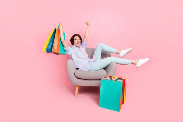 Volledige lengte lichaam grootte foto vrouw zitten in stoel houden pakketten gebaren als winnaar geïsoleerde pastel roze kleur achtergrond — Stockfoto