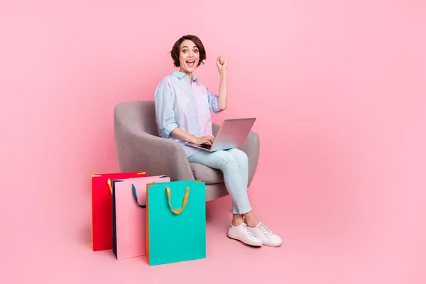 Longitud completa cuerpo tamaño foto mujer sentado con paquetes de trabajo en el gesto de la computadora como ganador aislado pastel color rosa fondo —  Fotos de Stock