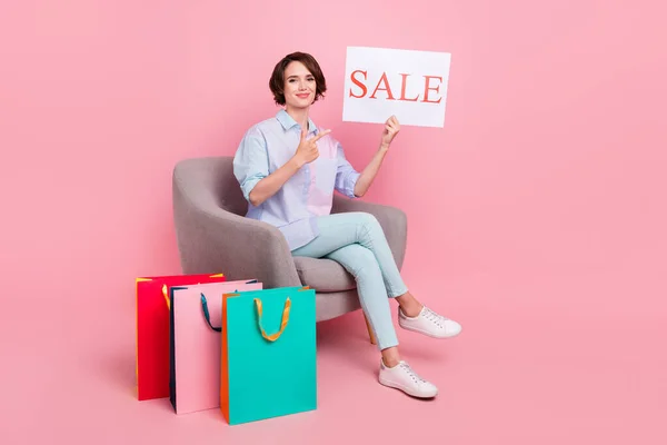 Ganzkörpergröße Foto Frau sitzt nach dem Online-Einkauf halten Verkaufskarte isoliert pastellrosa Farbe Hintergrund — Stockfoto