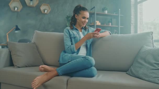 Positieve leuke leuke dame zitten gezellige bank sms 'en vrienden telefoon remote chat — Stockvideo