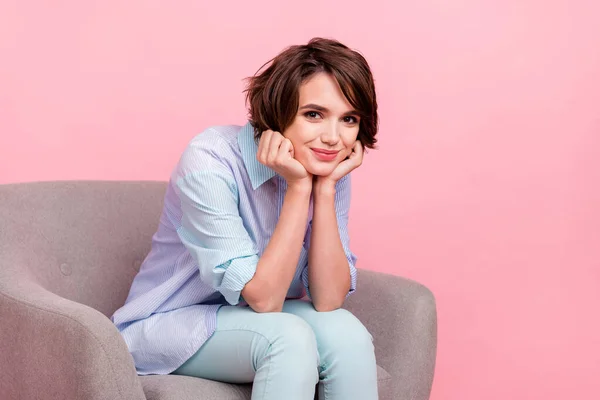 Foto retrato joven mujer de negocios sentada en sillón sonriendo en camisa a rayas aislado pastel color rosa fondo —  Fotos de Stock