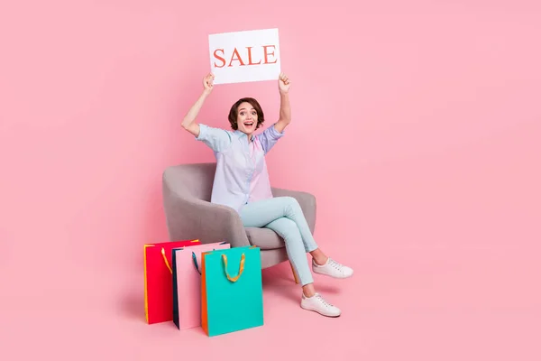 Ganzkörpergröße Foto Frau sitzt nach dem Online-Shopping erstaunt zeigt Verkauf Plakat isoliert pastellrosa Farbe Hintergrund — Stockfoto
