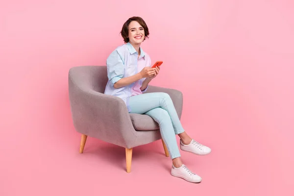 フル長さ体サイズ写真女性で座って椅子ブラウジングインターネット上の携帯電話隔離されたパステルピンク色の背景 — ストック写真