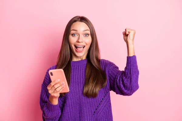 Фото оптимистичной девушки держать телефон кулак носить сиреневый свитер изолированы на пастельно-розовый цвет фона — стоковое фото