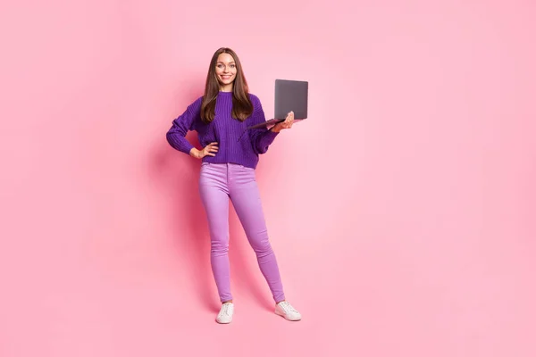 Foto de tamaño completo de chica optimista mantenga portátil usar suéter lila pantalones zapatillas aisladas sobre fondo rosa —  Fotos de Stock