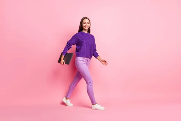 Πλήρης φωτογραφία προφίλ του αισιόδοξου κοριτσιού πάει να κρατήσει φορητό υπολογιστή φορούν λιλά παντελόνια πουλόβερ sneakers απομονώνονται σε ροζ χρώμα φόντο — Φωτογραφία Αρχείου