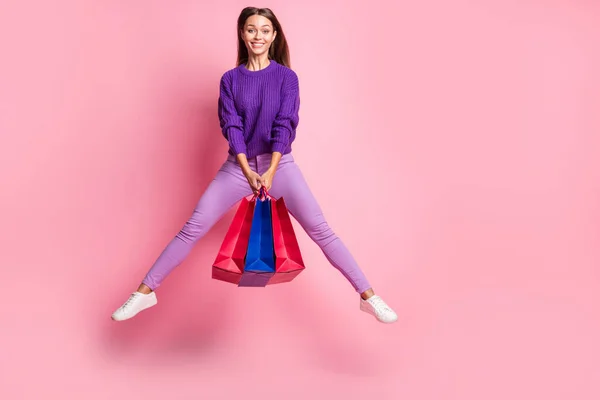 Фотографія оптимістичного стрибка дівчини тримайте сумку в бузковому светрі штани кросівки ізольовані на рожевому фоні — стокове фото