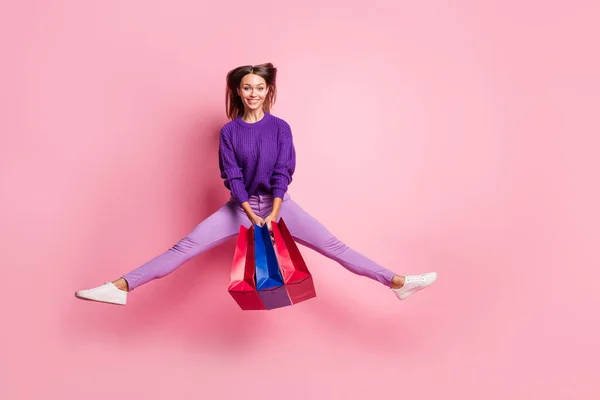 Retrato de cuerpo completo de persona alegre activa sostiene bolsas saltando las piernas a los lados se divierten aislados en el fondo de color rosa —  Fotos de Stock