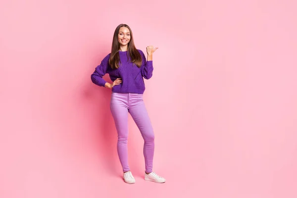 Full length φωτογραφία του κοριτσιού άμεσο αντίχειρα κενό χώρο φορούν βιολετί παντελόνι πουλόβερ sneakers απομονωμένο ροζ φόντο χρώμα — Φωτογραφία Αρχείου
