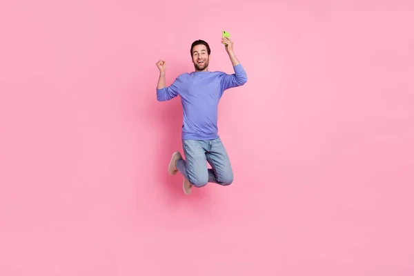 Full length photo of brunet cool millennial guy jump hold telefon nosić niebieskie trampki pullover izolowane na różowym tle — Zdjęcie stockowe