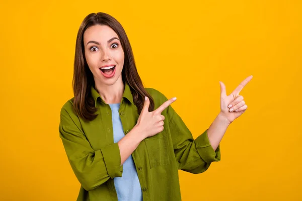 Foto van glanzend onder de indruk jonge dame dragen groene shirt wijzende vinger lege ruimte glimlachen geïsoleerde gele kleur achtergrond — Stockfoto