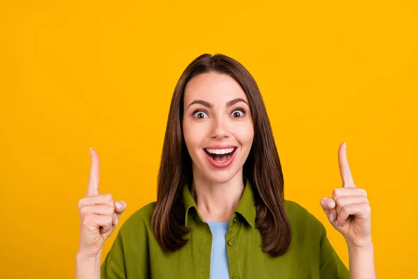 매력적 인 젊은 아가씨가 녹색 셔츠를 입고 빈 공간을 손가락으로 가리키며 누런 노란 배경을 웃고 있는 사진 — 스톡 사진