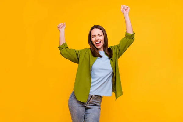 Foto de funky afortunada joven dama usar camisa verde sonriente bailando levantando puños aislado color amarillo fondo —  Fotos de Stock