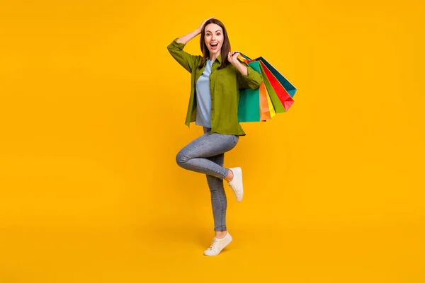 Foto de impressionado muito jovem senhora usar camisa verde sorrindo segurando sacos de compras braço cabeça isolado cor amarela fundo — Fotografia de Stock