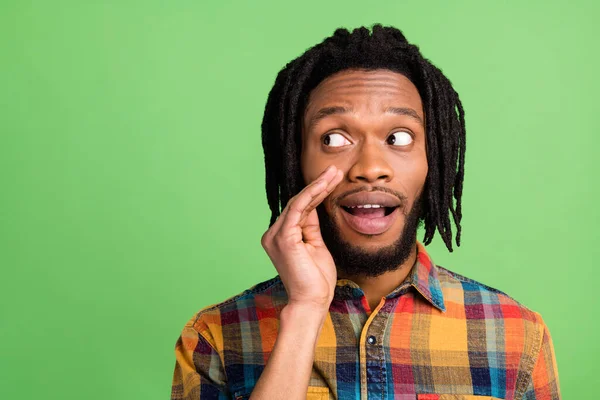 Foto de encantador chico de piel oscura complicado vestido camisa a cuadros labios del brazo diciendo secreto buscando espacio vacío aislado color verde fondo — Foto de Stock