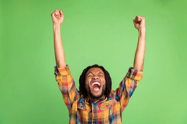 Photo of excited lucky dark skin man wear plaid shirt smiling rising fists isolated green color background — Stock Photo, Image