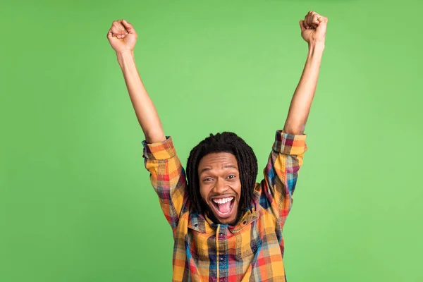 Photo of lucky funky dark skin guy dressed checkered shirt rising fists smiling isolated green color background — Stock Photo, Image
