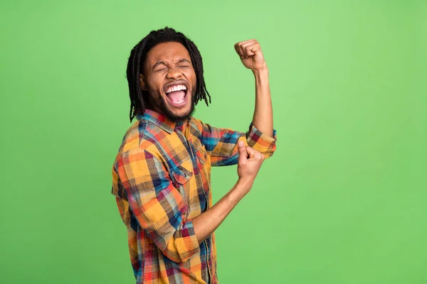 Foto de chico de piel oscura asombrado de ensueño vestido camisa a cuadros levantando puños sonriendo aislado color verde fondo —  Fotos de Stock