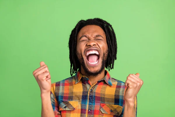 Photo of astonished lucky dark skin guy dressed checkered shirt rising fists smiling isolated green color background — Stock Photo, Image