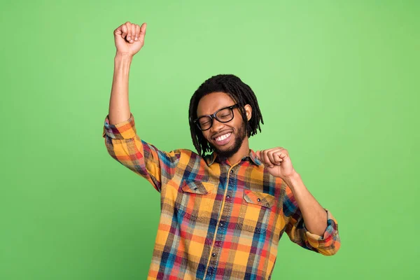 Foto van gelukkige funky donkere huid man dragen geruite shirt bril glimlachende rijzende vuisten dansen geïsoleerde groene kleur achtergrond — Stockfoto