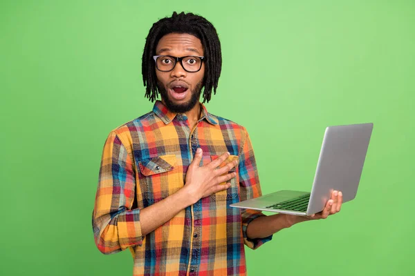 Fotografie užaslý na volné noze chlap držet netbook otevřená ústa nosit kostkované tričko izolované zelené barvy pozadí — Stock fotografie