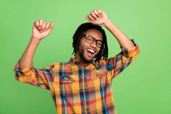 Фотография счастливчика довольно темная кожа парень одет клетчатые рубашки очки танцуют поднимая кулаки улыбаясь изолированный зеленый цвет фона — стоковое фото