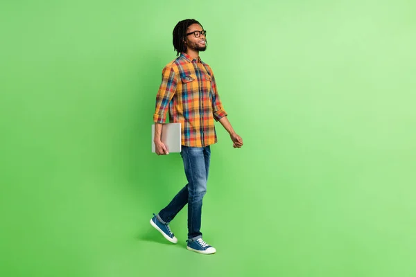 Foto de dulce confiado chico de piel oscura vestido camisa gafas caminando sosteniendo dispositivo moderno espacio vacío aislado color verde fondo — Foto de Stock