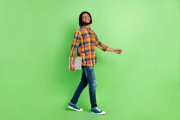 Foto de lindo hombre de piel bastante oscura usar gafas de camisa a cuadros sonriendo caminando sosteniendo gadget moderno aislado fondo de color verde — Foto de Stock