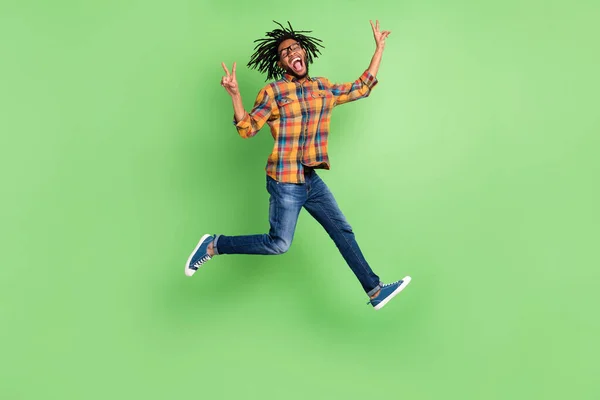 Foto de homem de pele escura muito funky usar óculos de camisa xadrez sorrindo pulando alto mostrando v-sinais isolado cor verde fundo — Fotografia de Stock
