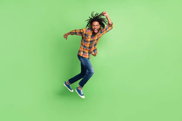 Photo of sweet excited dark skin guy dressed checkered shirt jumping high running fast smiling isolated green color background — Stock Photo, Image