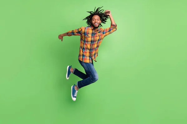 Foto de homem de pele escura encantador funky usar camisa xadrez sorrindo saltando alto apressando isolado fundo cor verde — Fotografia de Stock