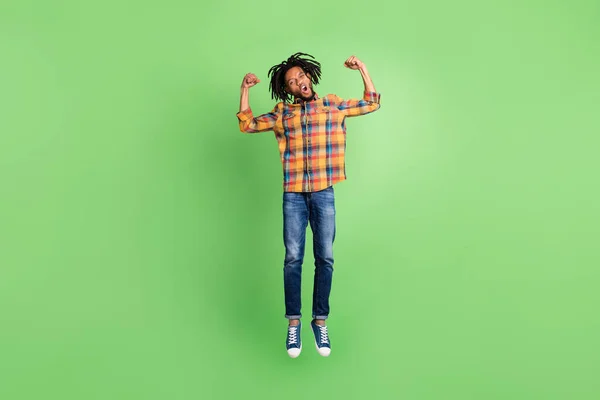 Foto do cara pele muito escura animado vestido camisa quadriculada saltando alto mostrando punhos sorrindo isolado fundo cor verde — Fotografia de Stock