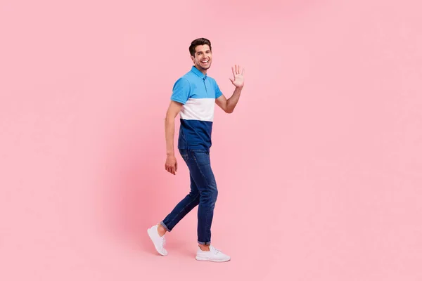 Full body profile photo of joyful brunet millennial guy go wave wear polo jeans sneakers isolated on pink background
