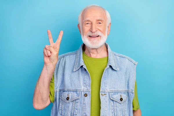 Φωτογραφία του funky χαριτωμένο συνταξιούχος φορούν vintage τζιν γιλέκο δείχνει v-σημάδι χαμογελώντας απομονωμένο μπλε χρώμα φόντο — Φωτογραφία Αρχείου