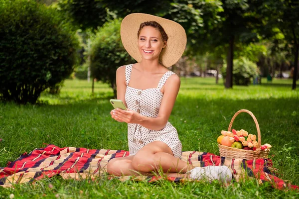 Foto de comprimento total de encantador jovem feliz mulher positiva segurar as mãos telefone sentar cobertor piquenique ao ar livre fora do parque — Fotografia de Stock