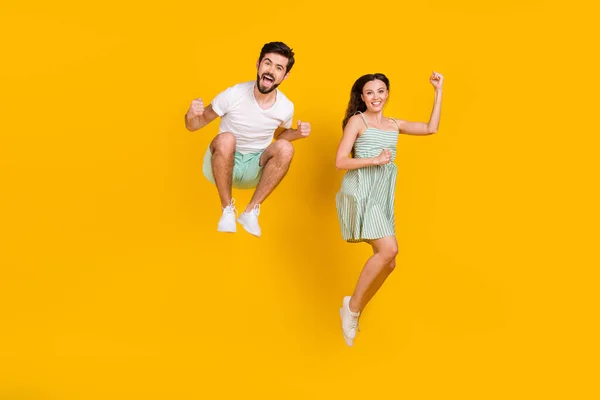 Fénykép őrült házaspár emelje ököllel ugrás elérni cél viselése alkalmi ruhát elszigetelt sárga színű háttér — Stock Fotó
