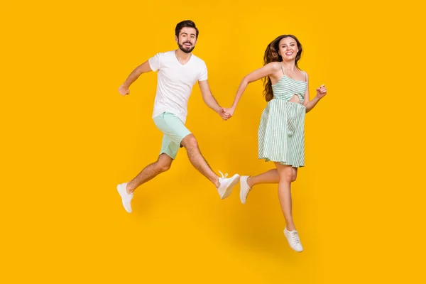 Photo de fou couple actif sauter tenir la main profiter de vol porter tenue décontractée isolé couleur jaune fond — Photo