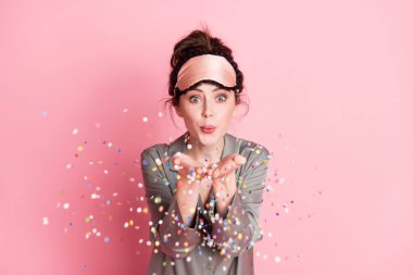Photo portrait of girl in sleeping mask blowing sequins on pajama party isolated on pastel pink color background clipart