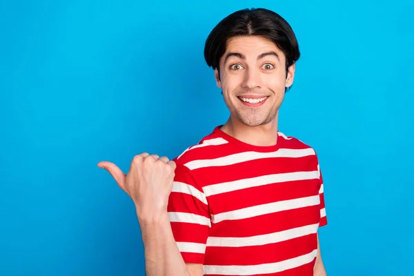 Photo de charmant jeune homme impressionné habillé rouge t-shirt pointant pouce retour espace vide sourire isolé fond de couleur bleue — Photo