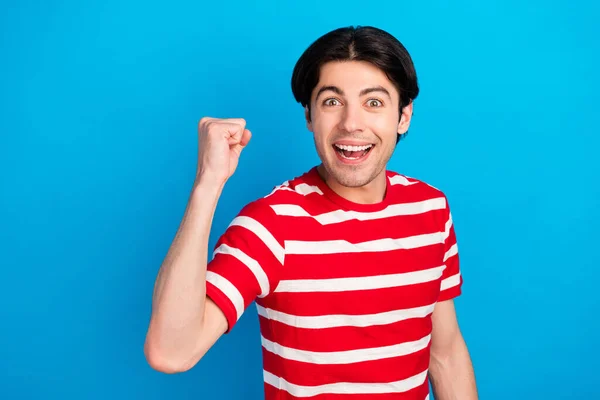 Foto van zoete funky jongeman dragen gestreepte t-shirt glimlachen stijgende vuist geïsoleerde blauwe kleur achtergrond — Stockfoto