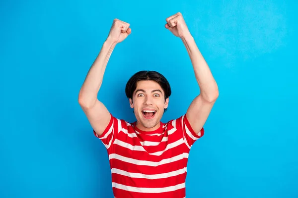 Foto van onder de indruk glanzende jonge man gekleed rood t-shirt rijzende vuisten glimlachen geïsoleerde blauwe kleur achtergrond — Stockfoto