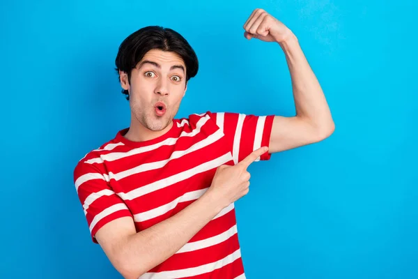Foto van sterke onder de indruk jonge man gekleed rood t-shirt wijzend vinger biceps geïsoleerde blauwe kleur achtergrond — Stockfoto