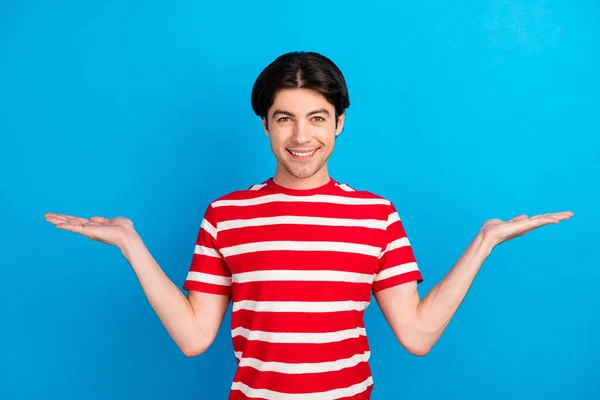 Photo de doux charmant jeune homme porter rayé t-shirt comparer les bras espace vide sourire isolé fond de couleur bleue — Photo