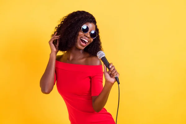 Foto de la joven hermosa impresionante chica afro positivo en gafas de sol cantando karaoke aislado en el fondo de color amarillo — Foto de Stock