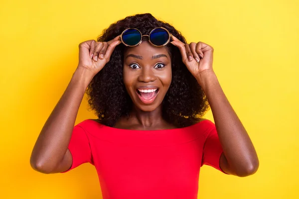 Foto de joven feliz emocionado loco afro chica ver gran venta de descuento usar gafas de sol aisladas en el fondo de color amarillo —  Fotos de Stock