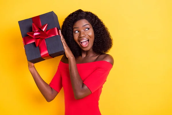 Photo of young happy excited smiling amazed girl shaking box guessing present isolated on yellow color background