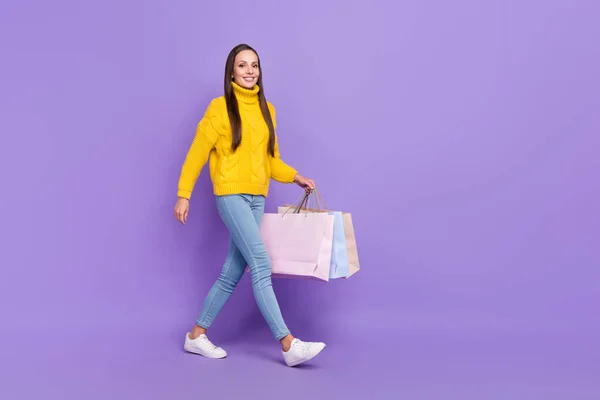 Full size foto van lachende vrouw gaan winkelen met volle zakken dragen denim jeans geïsoleerd op violette kleur achtergrond — Stockfoto