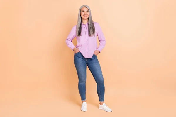 Full body photo of nice grey grey hairdo lady stand wear violet outfit jeans footwear isolated on beige color background — ストック写真