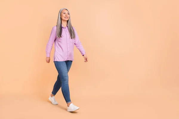 Full body photo of optimistic grey hairdo old lady go wear violet apparel jeans sneakers isolated on beige background —  Fotos de Stock
