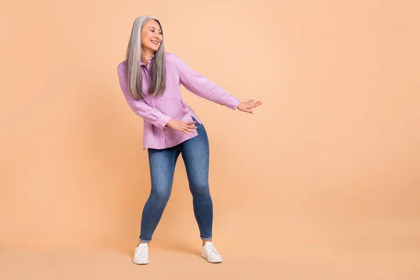 Фотографія повного тіла прохолодного сірого волосся стара леді танцює носить фіолетові сорочки джинси взуття ізольовані на бежевому фоні — стокове фото